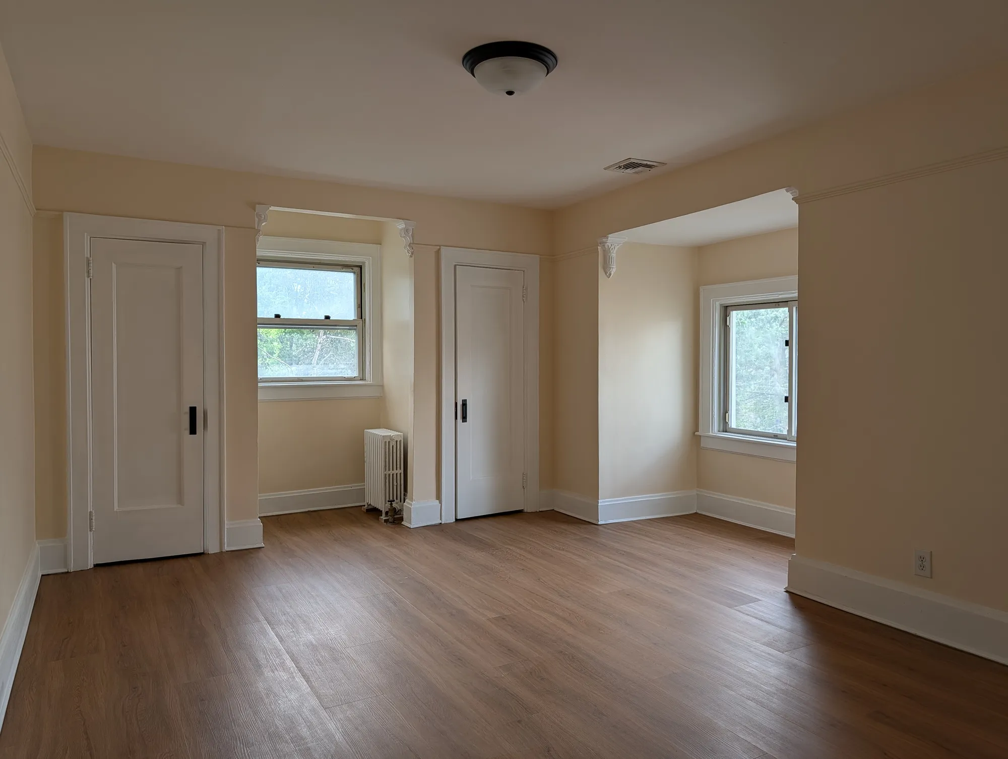 A second-floor bedroom with paired windows, two closet doors, and original corbels above the doorways over warm floors