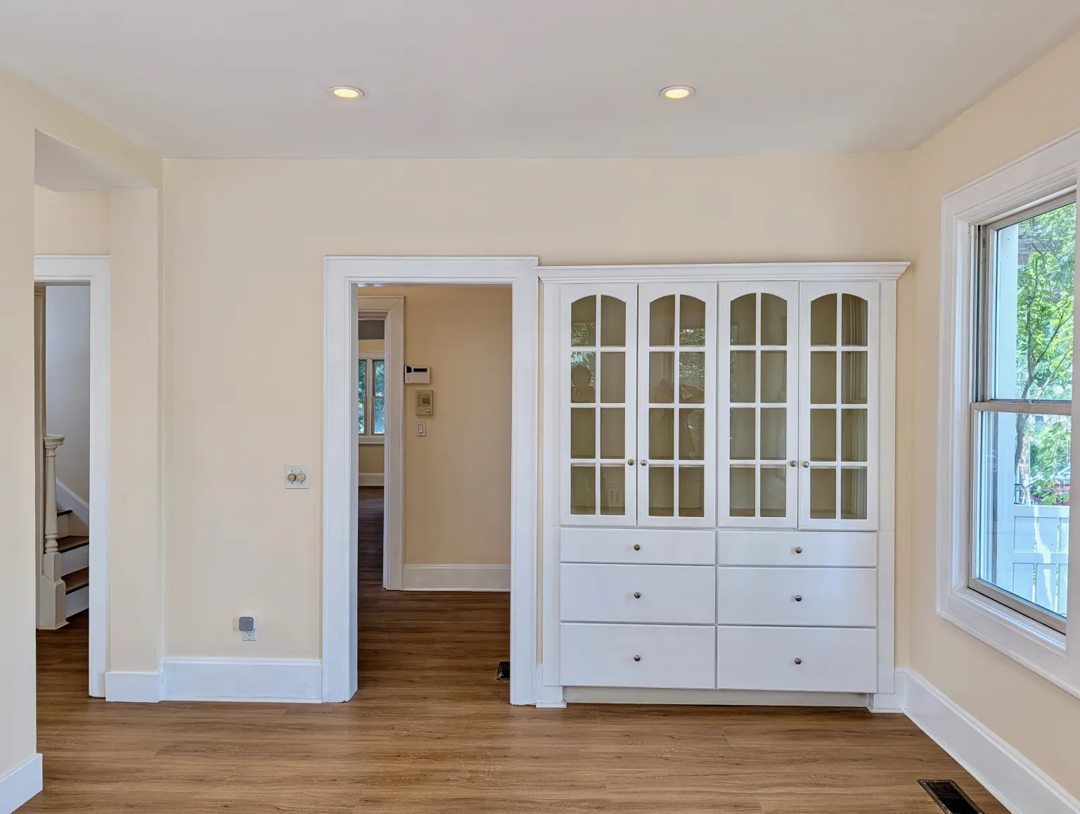 The built-in china cabinet with four arched glass doors over six drawers, beside a tall window onto the side yard