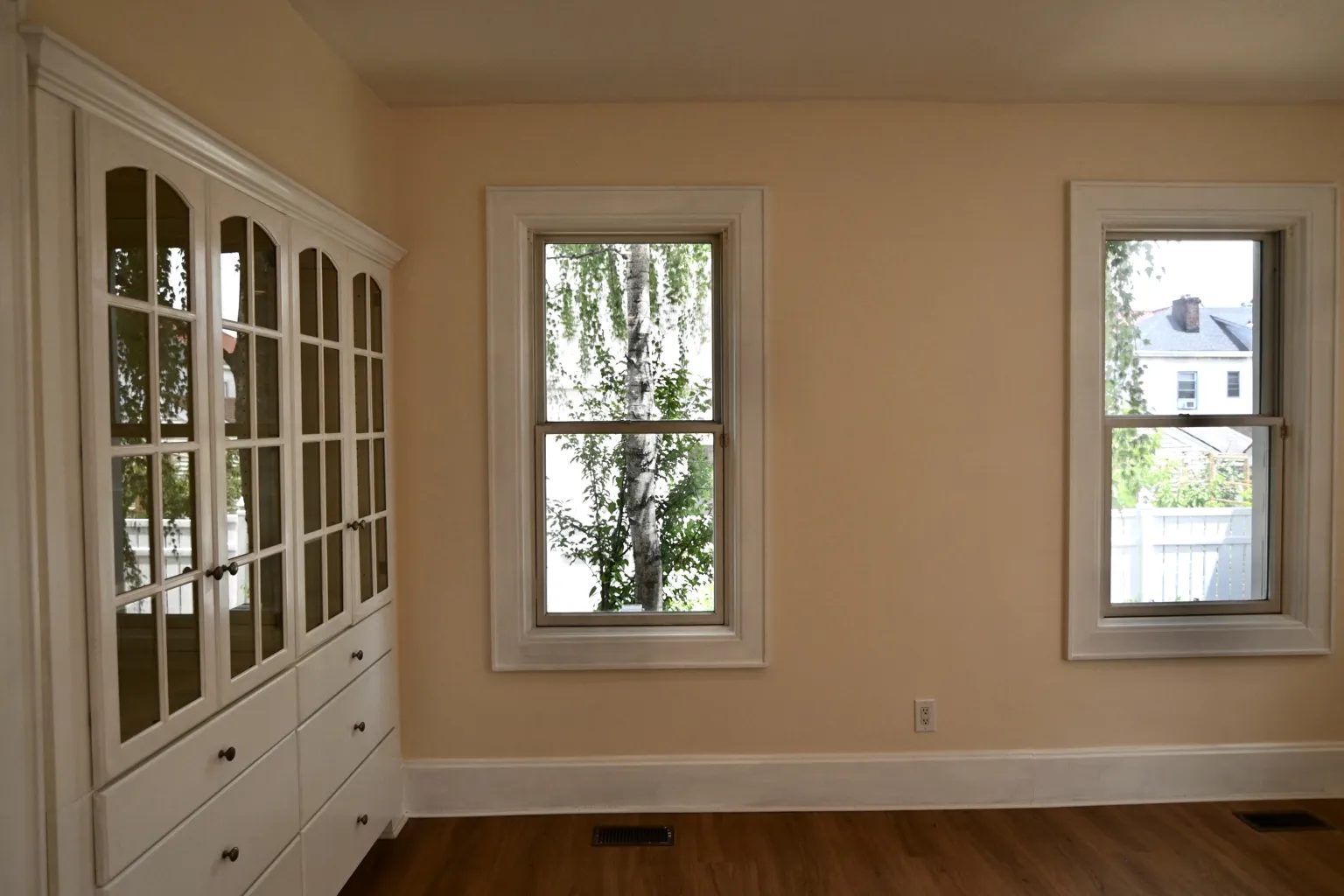 The dining room corner with the built-in china cabinet on one wall and two tall windows on the adjacent wall looking onto the trees outside