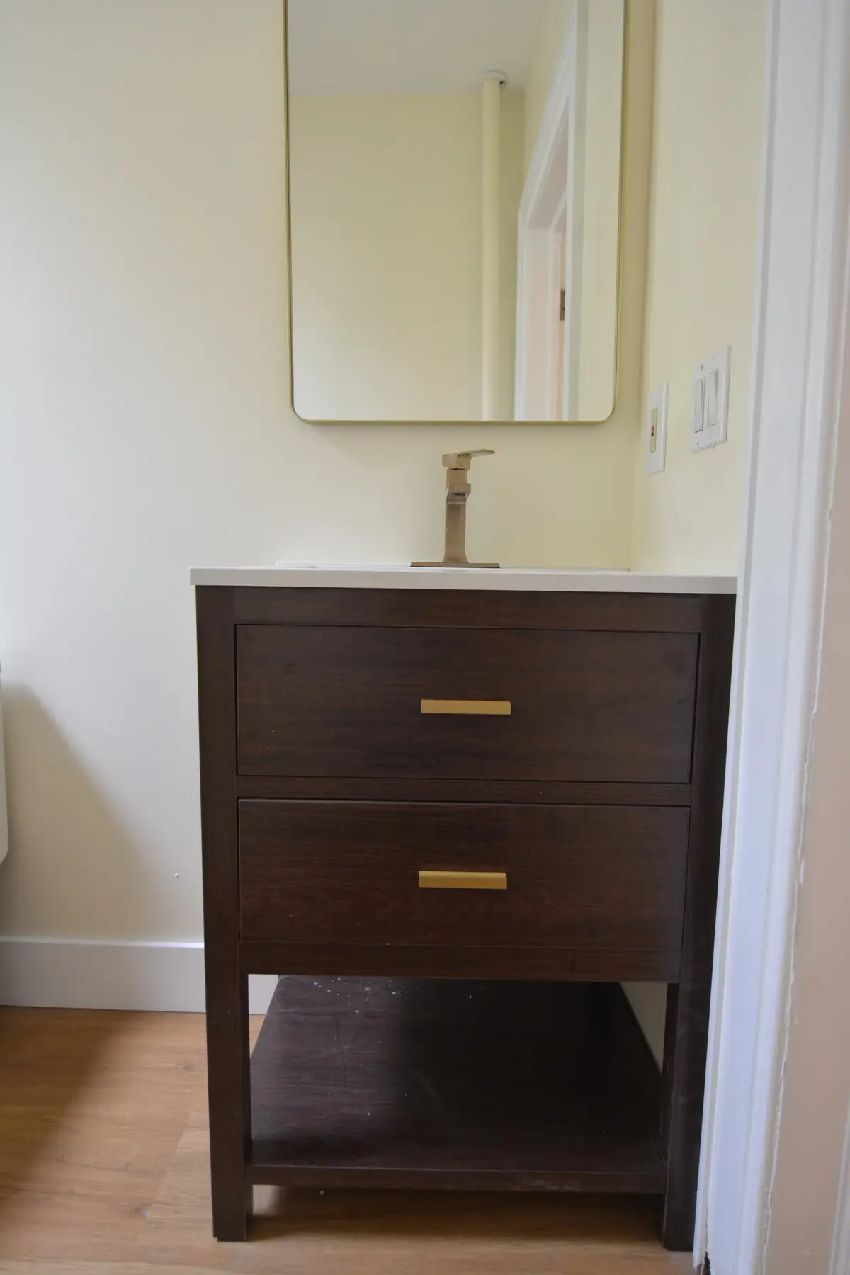 Closer view of the half-bath dark-wood vanity with brass pulls and brass faucet