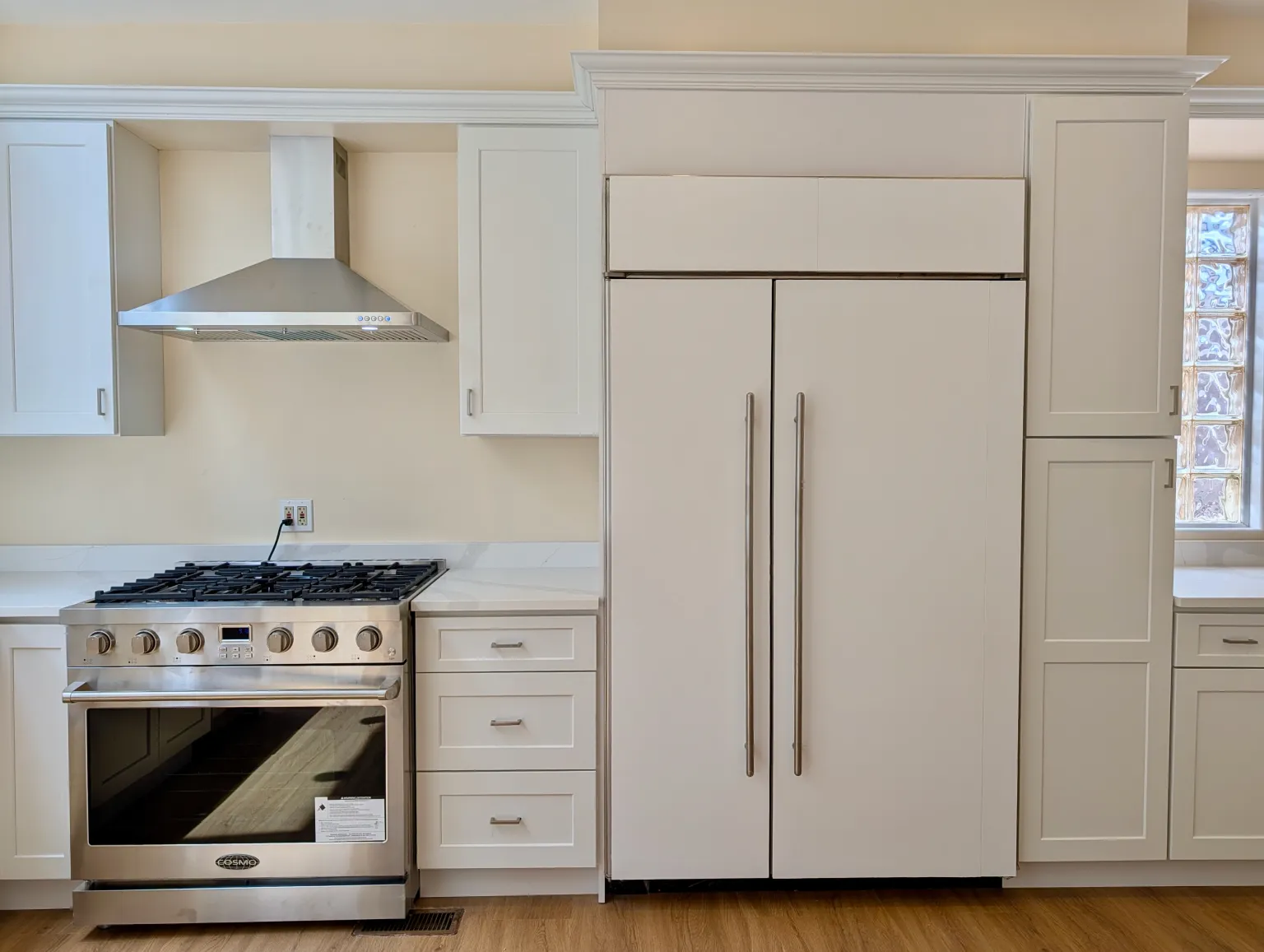 The stainless gas range and vented hood beside the panel-front refrigerator and a tall pantry cabinet