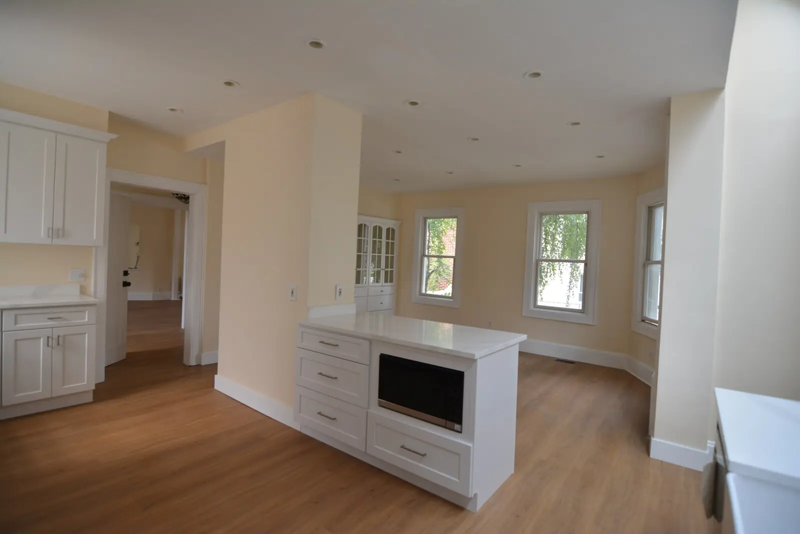 Looking from the kitchen across the peninsula into the dining corner, paired windows on two walls, the china cabinet visible alongside
