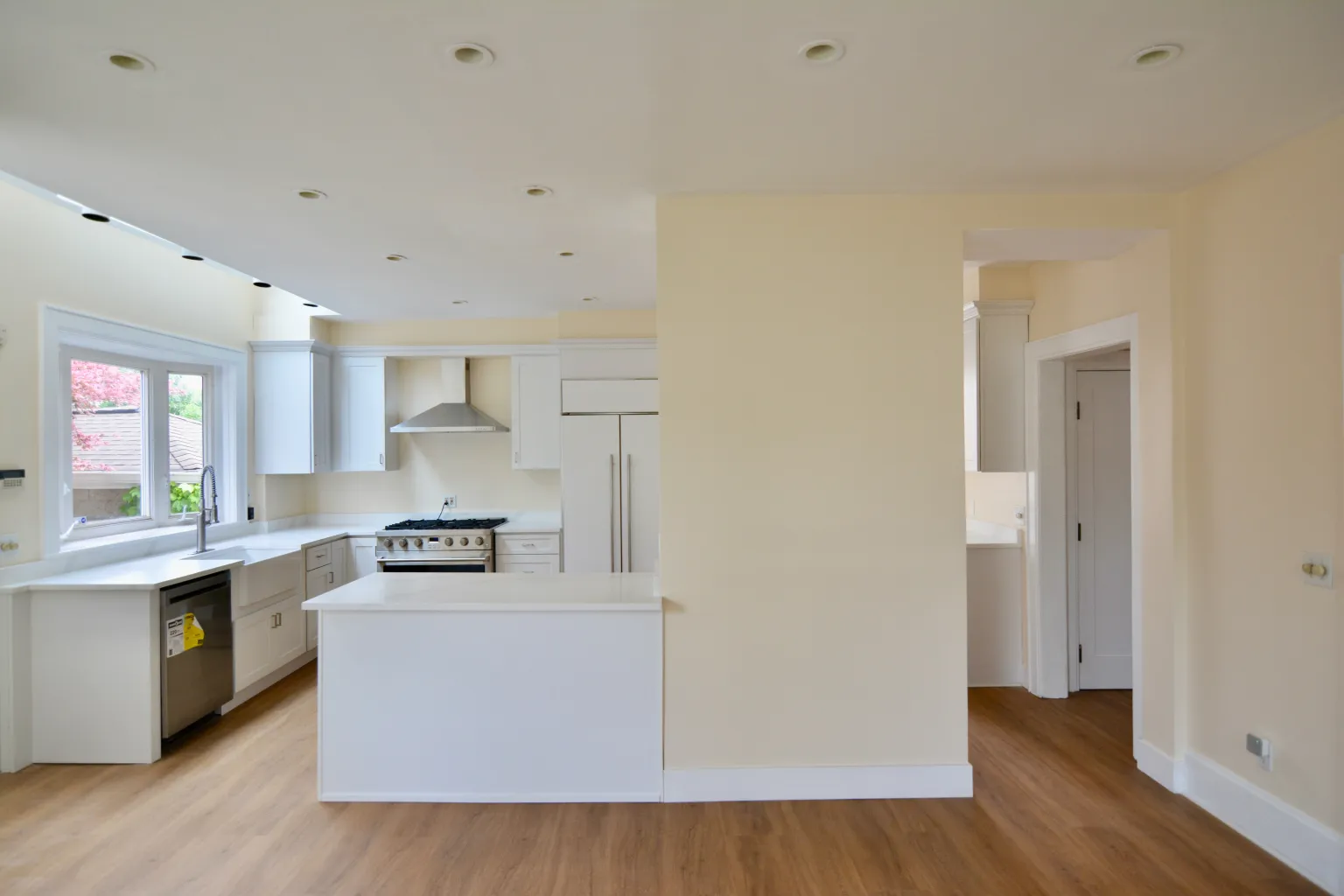 Wide kitchen view from the dining side showing sink, range, fridge, and sightline through to the entry