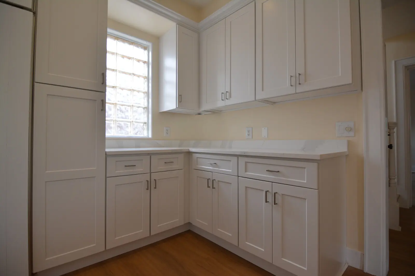 A pantry counter beside the refrigerator with shaker cabinets and a glass-block window