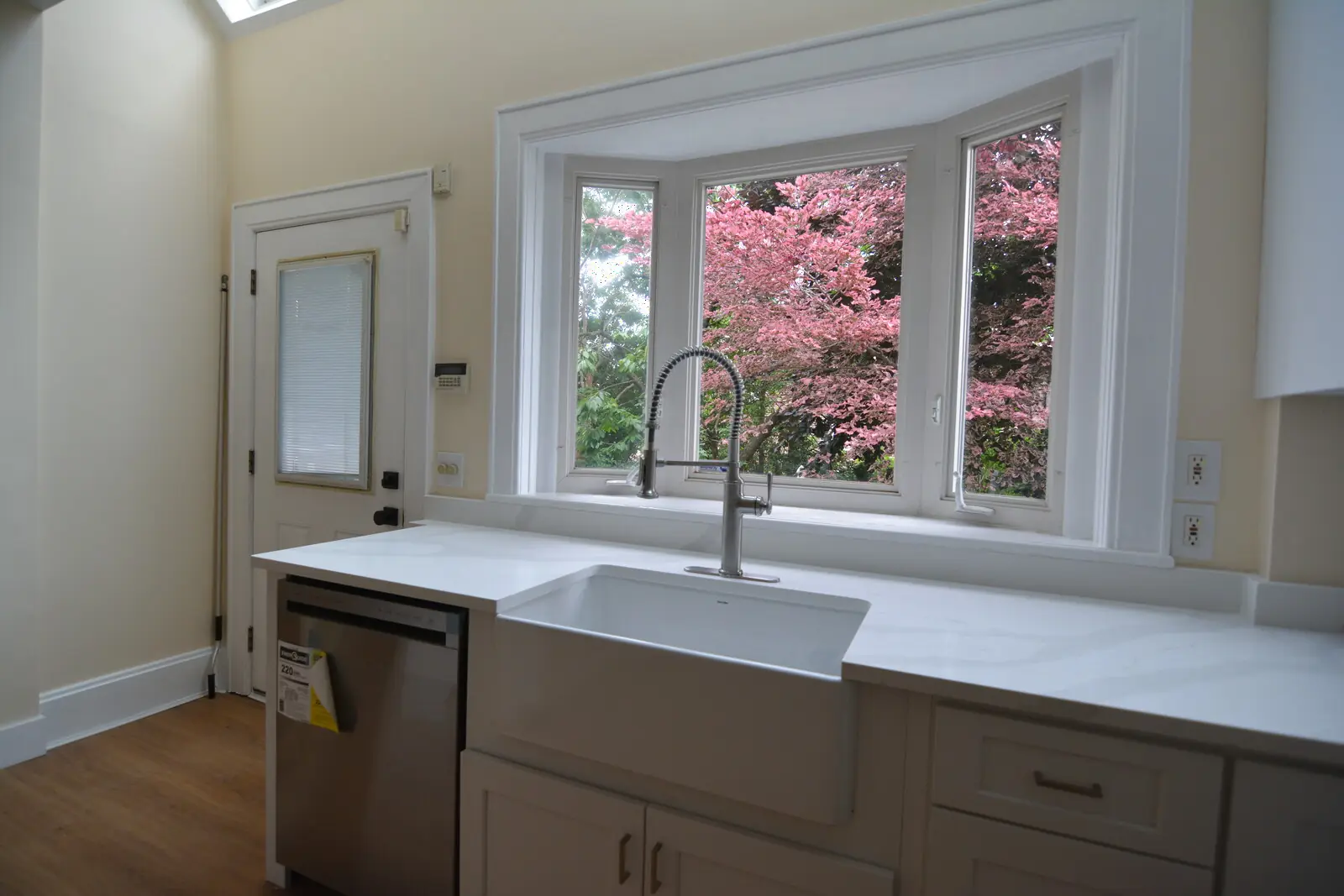 The apron-front sink under the three-pane bay window onto the red-leaved beech