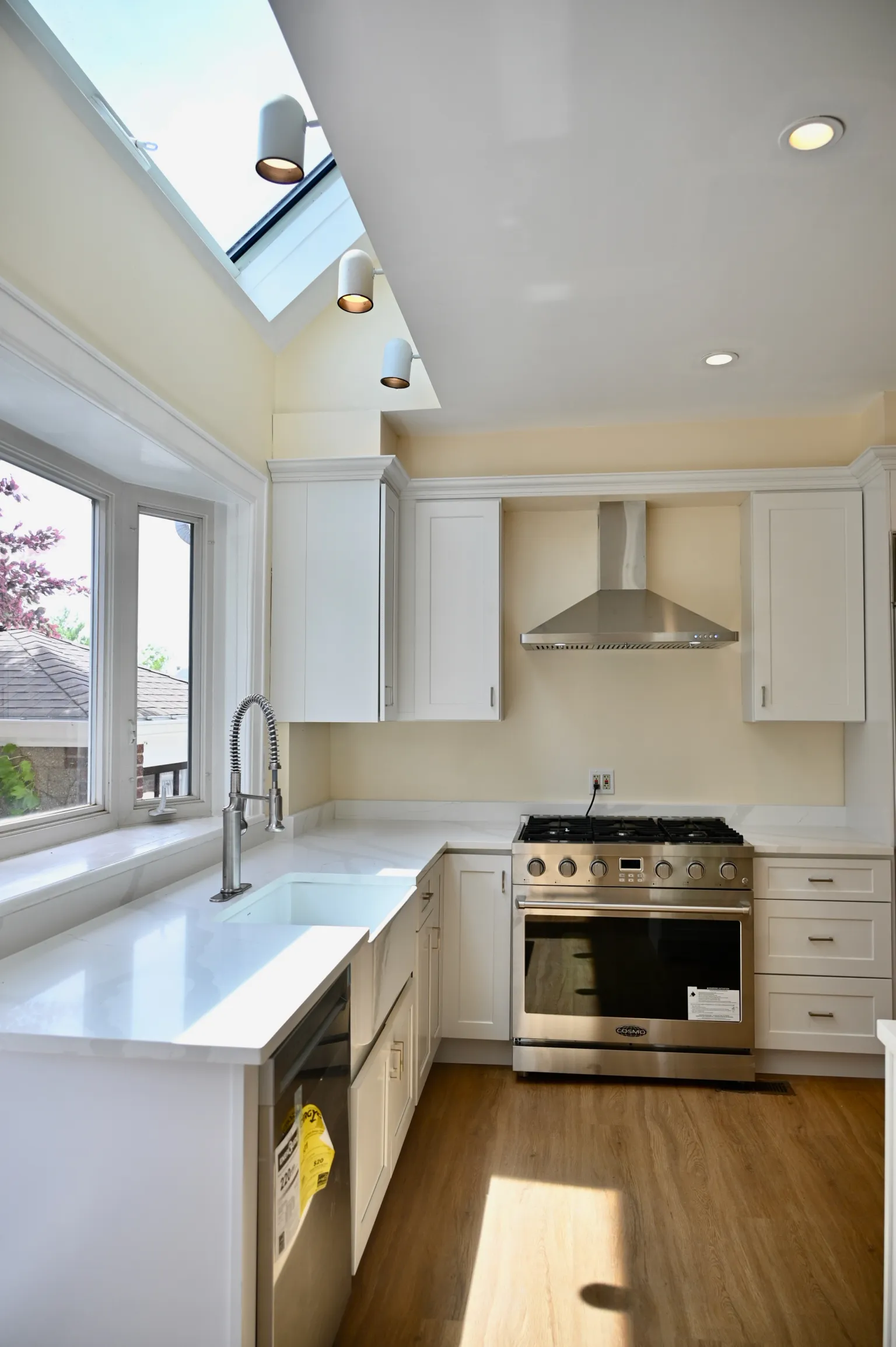 The kitchen under a long skylight set into the sloped ceiling, pendant lights below, with the apron sink and bay window at left and the stainless gas range and vented hood at right