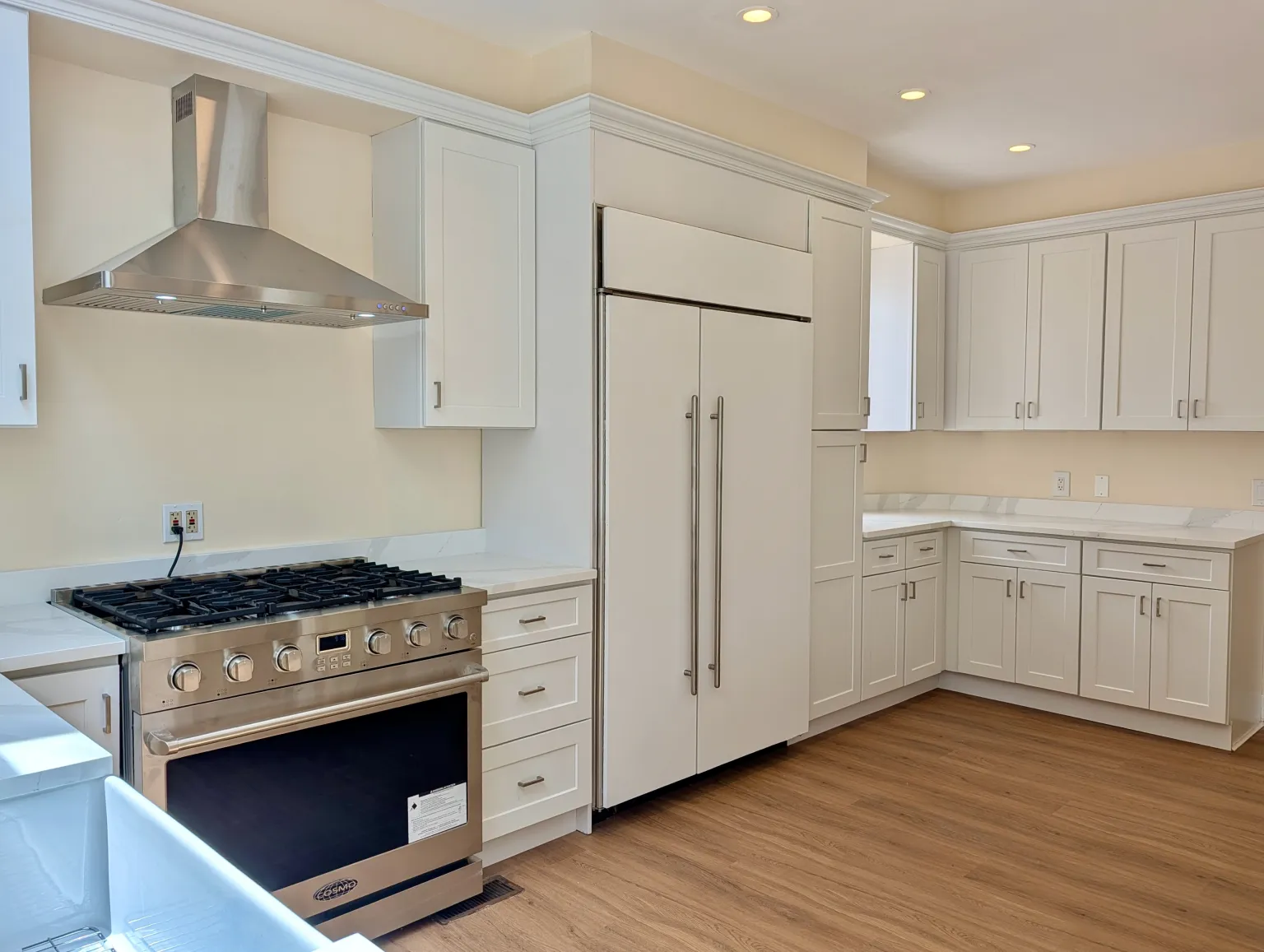 Wider kitchen view from the sink side, the stainless range and hood at left and the panel-front refrigerator with the cabinet run wrapping the corner
