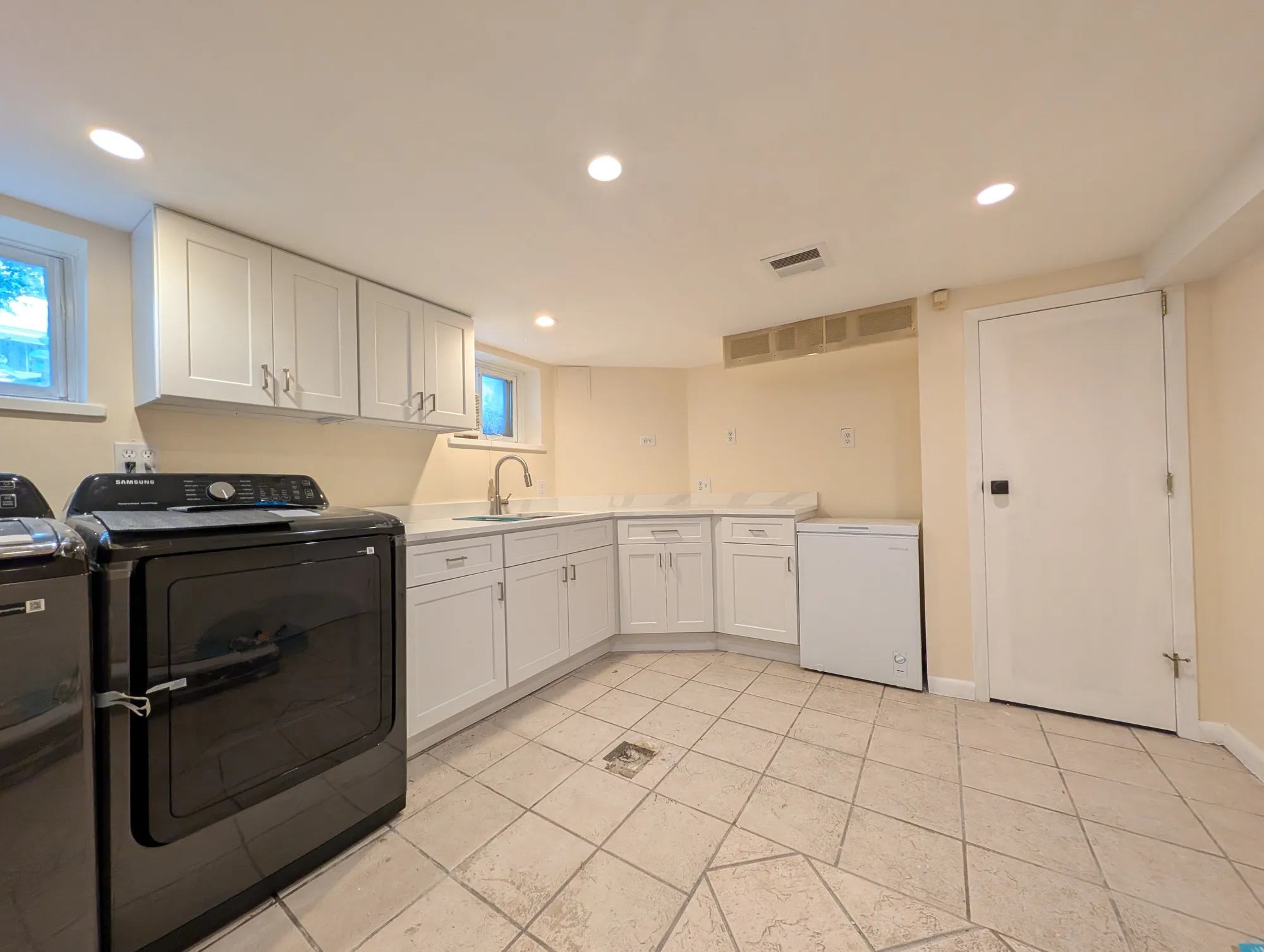 The laundry and utility area built into the back corner of the lower level, shaker cabinets, corner sink, washer/dryer, and a chest freezer