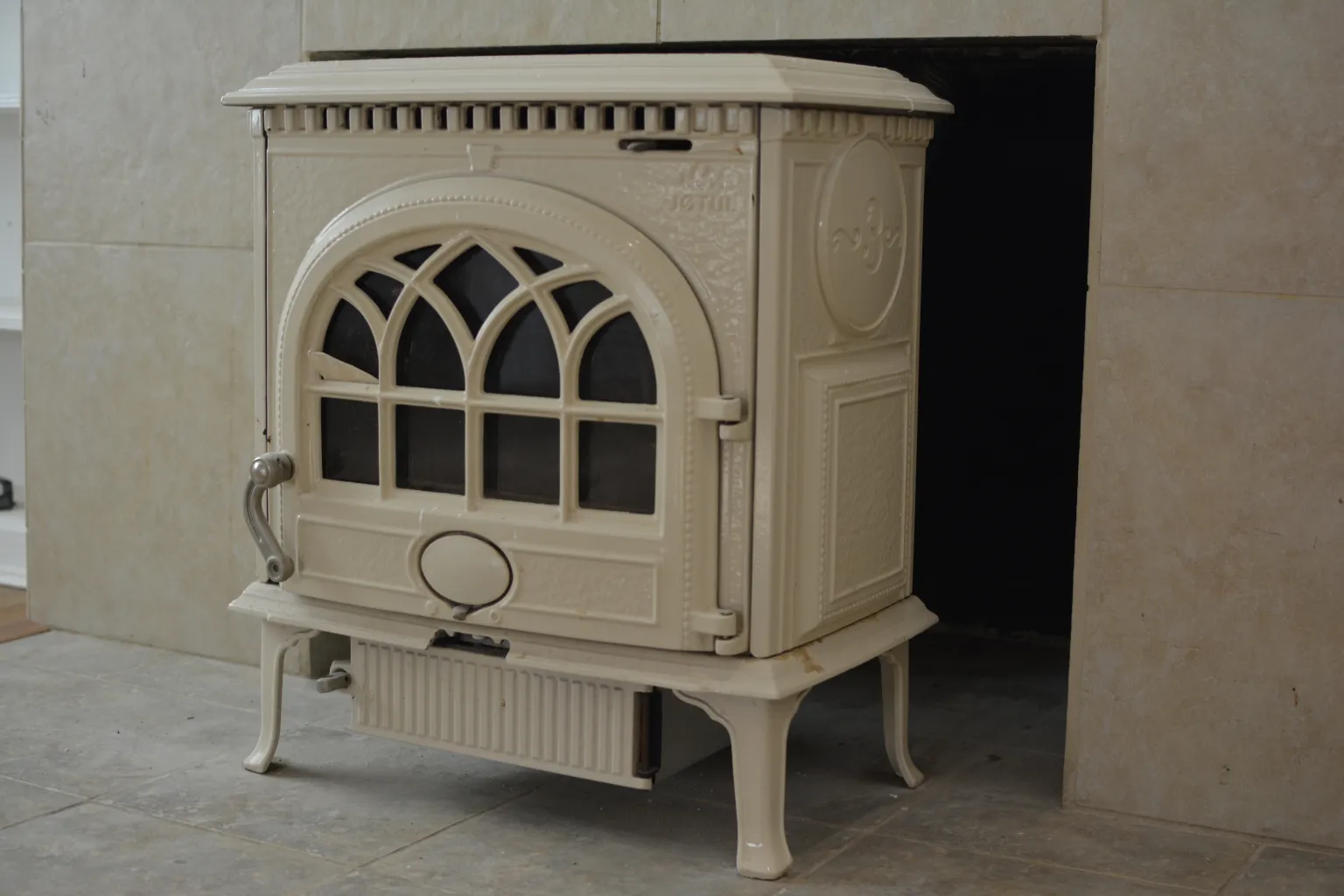 Cream enameled stove with an arched glass door set into a tiled hearth