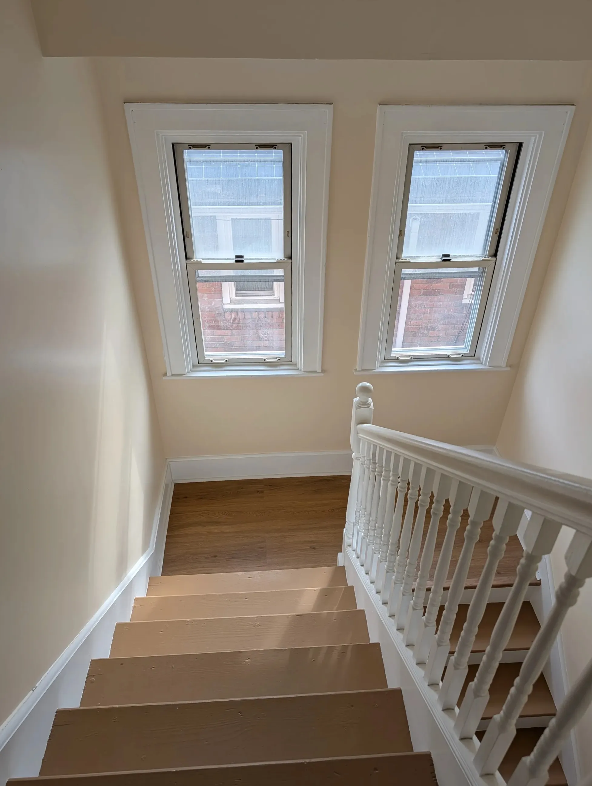 Looking down the staircase from the second-floor landing toward the main floor, with twin windows above the landing