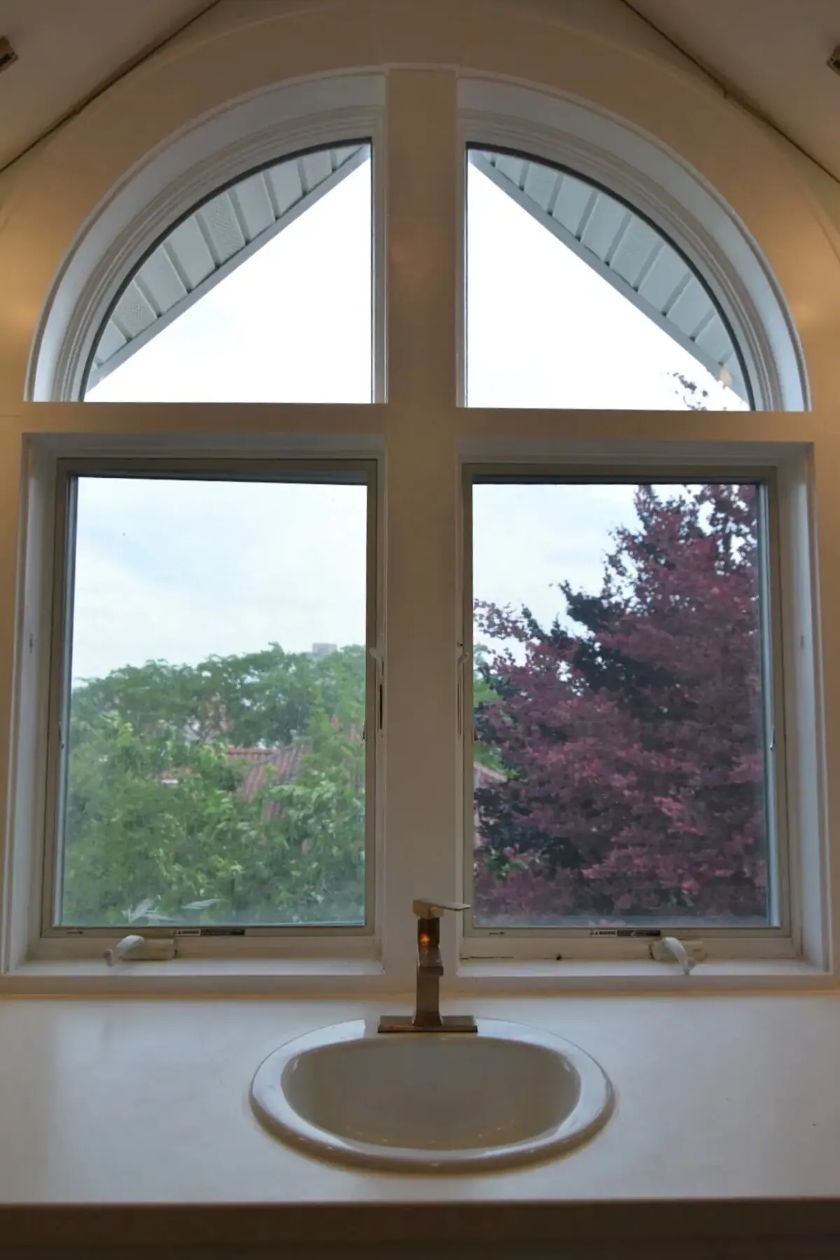 The suite bath sink and brass faucet beneath the south arched window, looking out on the red-leaved beech in the back yard