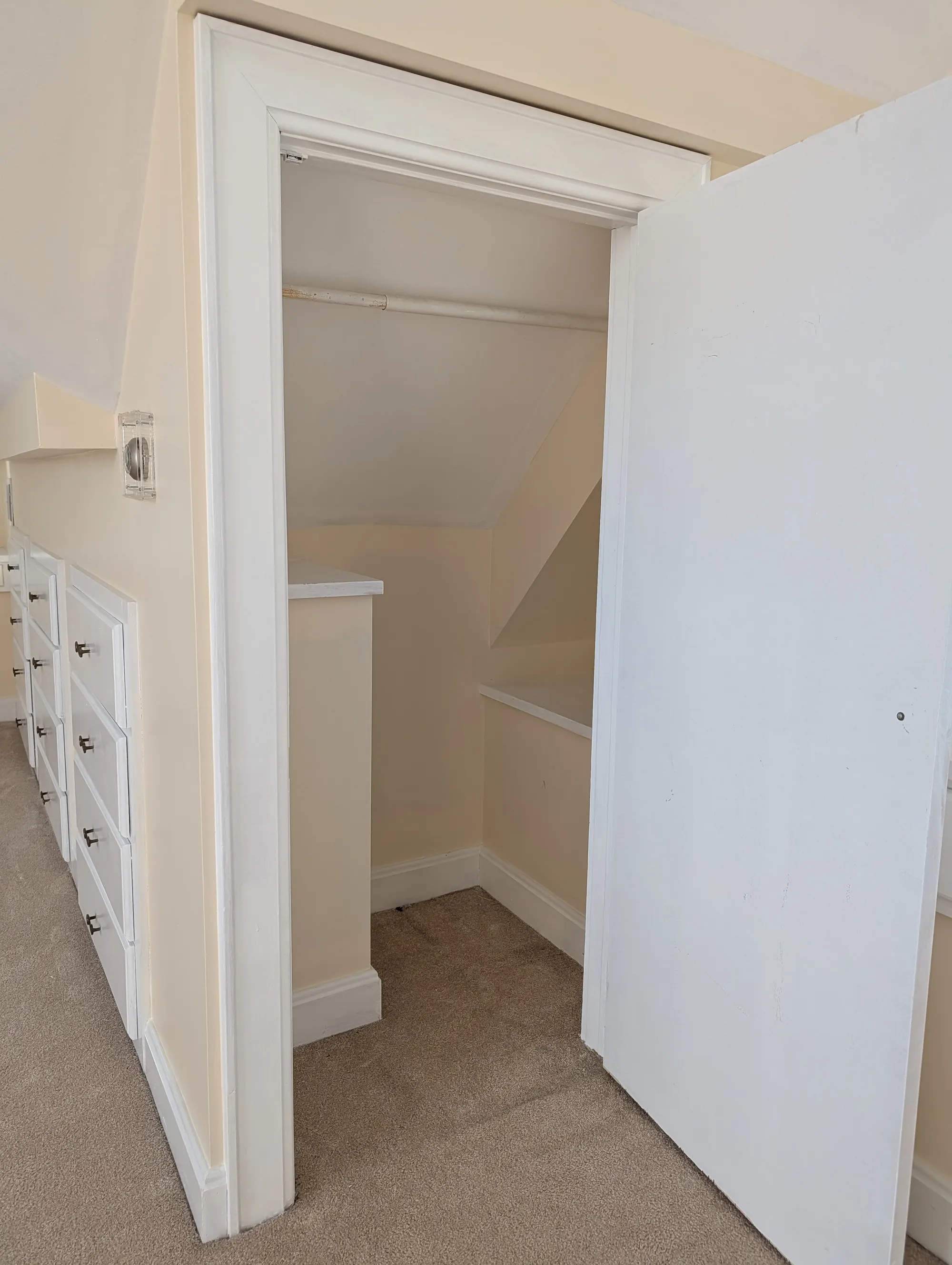 A closet opening beside the built-in chest of drawers on the suite floor, with a hanging rod inside