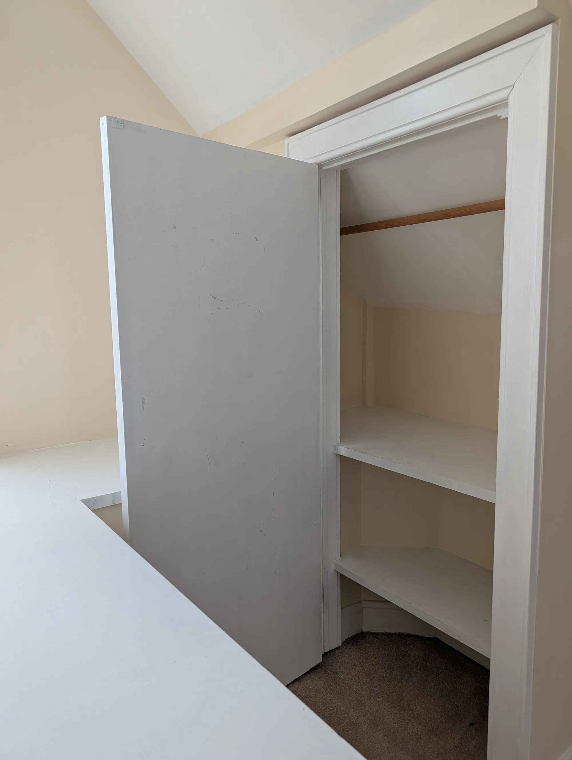 A closet built into the suite eave, shaped to the slope of the vaulted ceiling, with a hanging rod above and stepped shelves following the roofline down