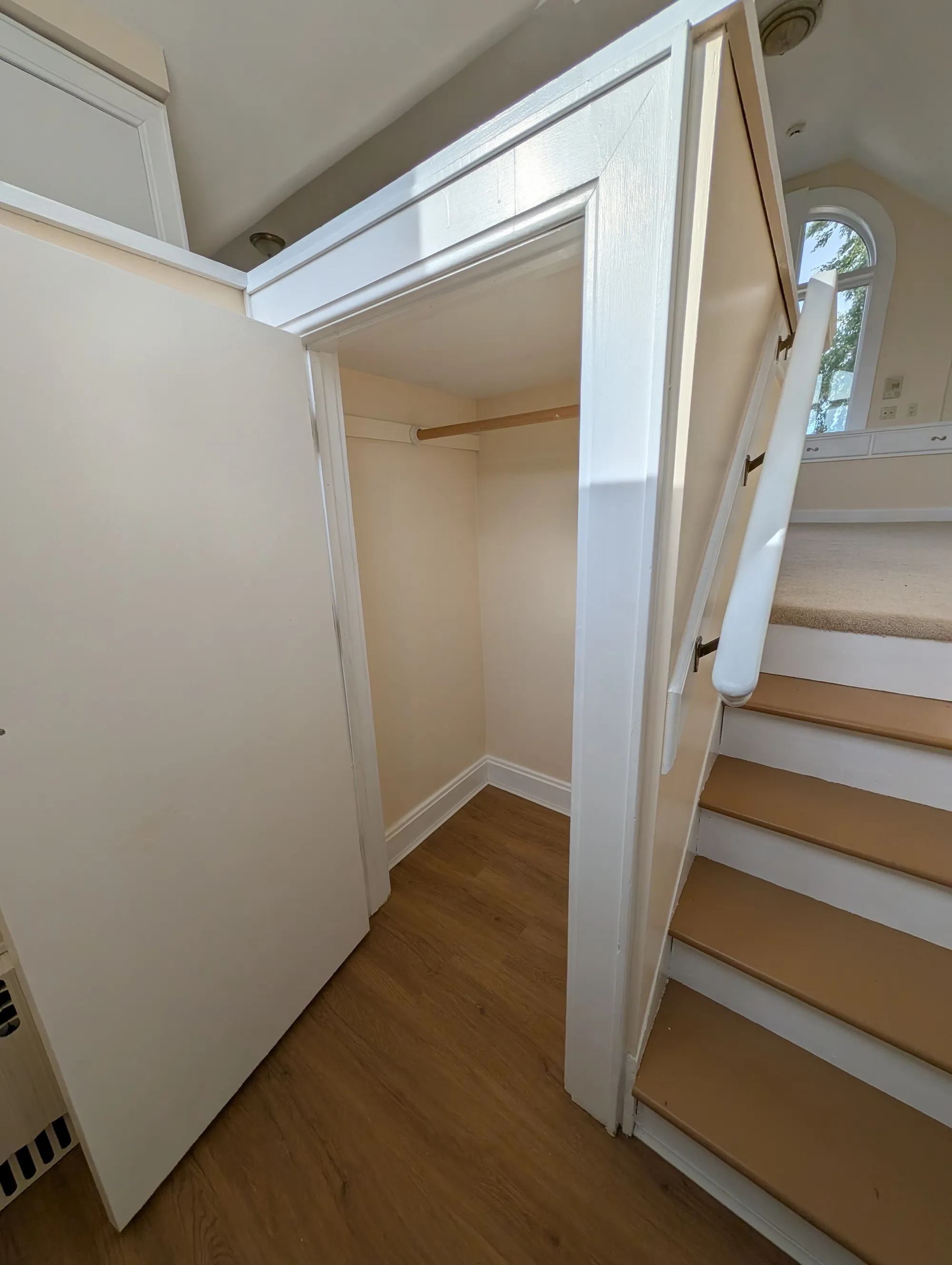 A storage closet tucked alongside the staircase up to the suite, with the arched window visible at the landing above