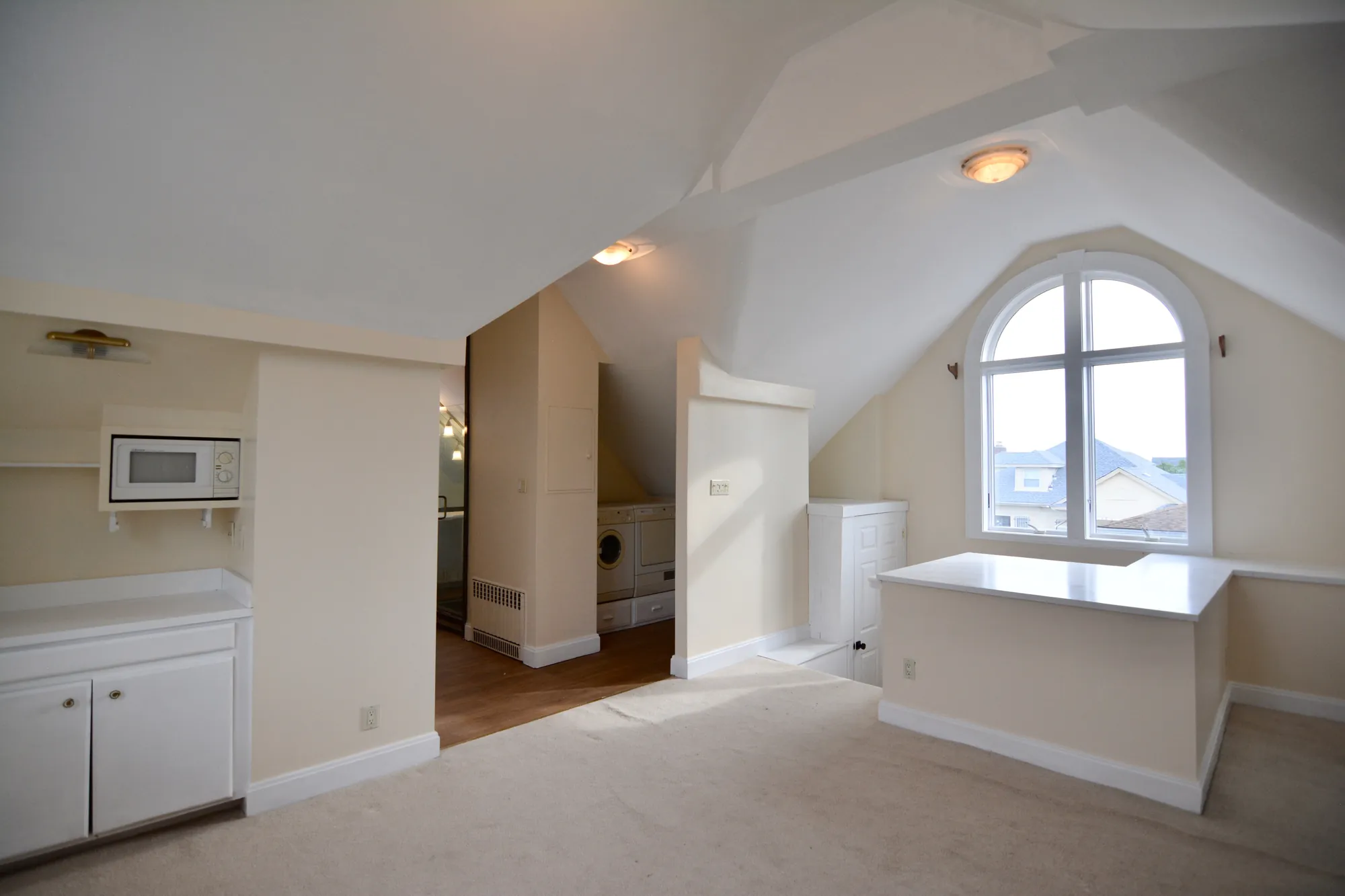 The southwest corner of the suite, kitchenette cabinetry along the wall, the washer/dryer alcove behind, and the west arched window at the far end