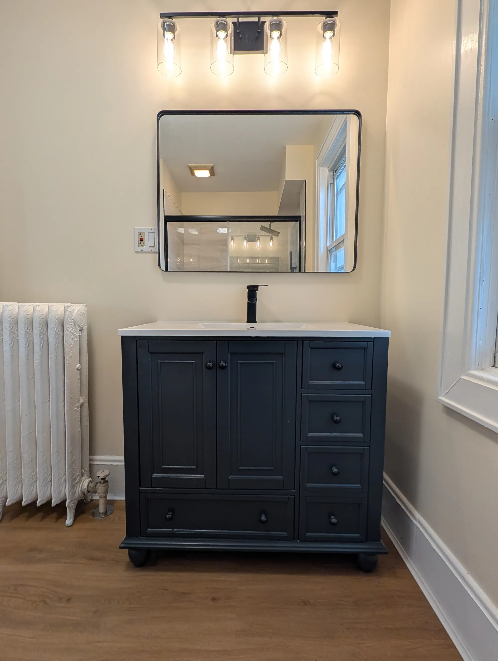 Second-floor full bath vanity, dark-wood cabinet with brass fixtures, a rectangular mirror with the glass shower reflected, and Edison-bulb sconces above